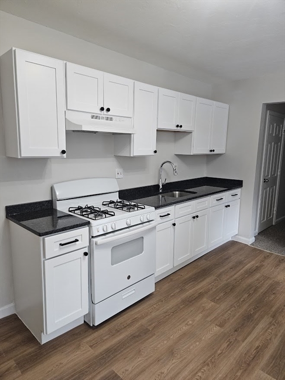 a white kitchen with granite countertop a stove top oven a sink and white cabinets with wooden floor