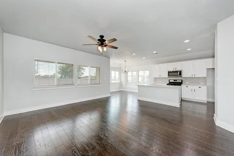 a view of an empty room with wooden floor and a kitchen