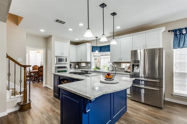 a kitchen with stainless steel appliances a refrigerator a stove a sink dishwasher a oven and a dining table with wooden floor