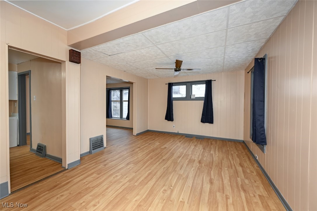 667 Elma Street Akron, OH 44310 - Photo 11 of 42 Empty room with ceiling fan, light wood-style flooring, wood walls, and a drop ceiling