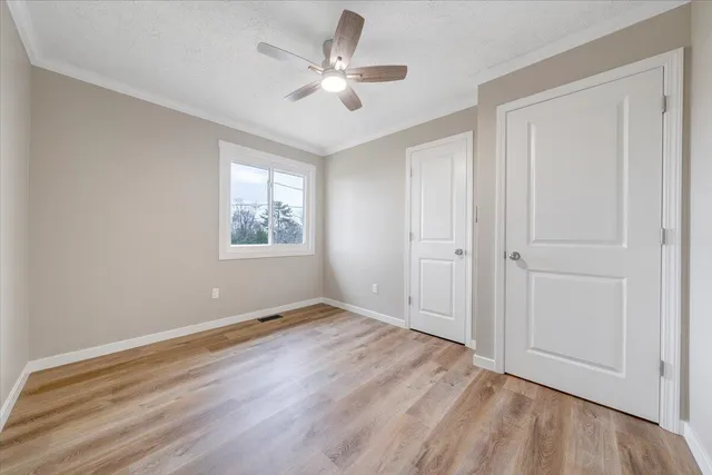 an empty room with wooden floor ceiling fan and windows