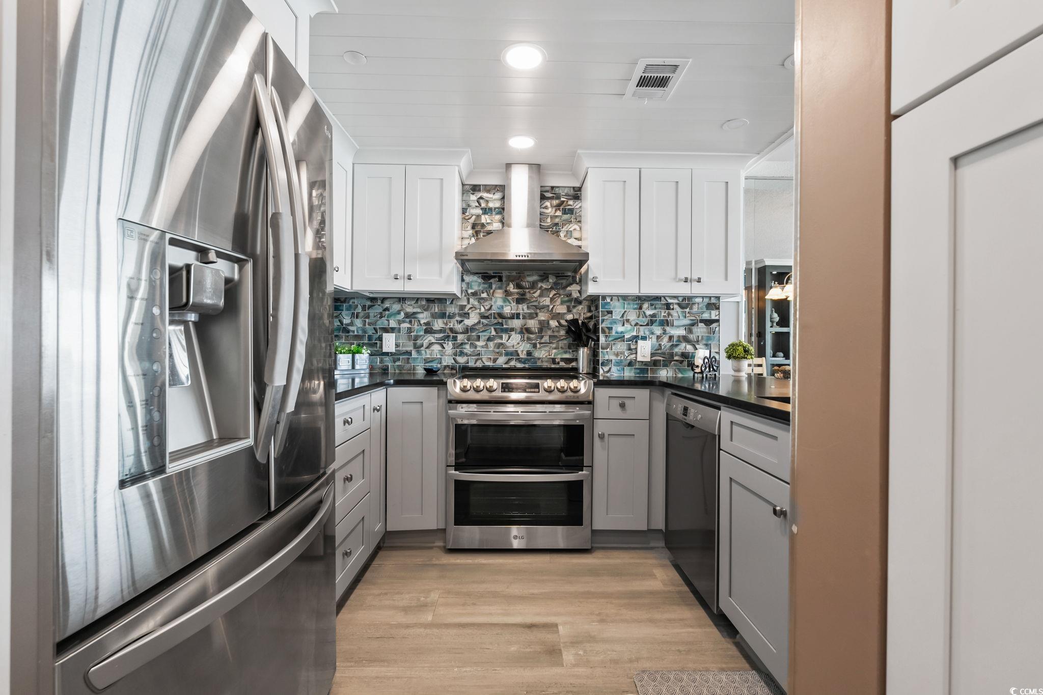 1990 North Waccamaw Drive, Unit 403 Murrells Inlet, SC 29576 - Photo 20 of 39 Kitchen featuring appliances with stainless steel finishes, gray cabinetry, backsplash, wall chimney range hood, and light wood-type flooring