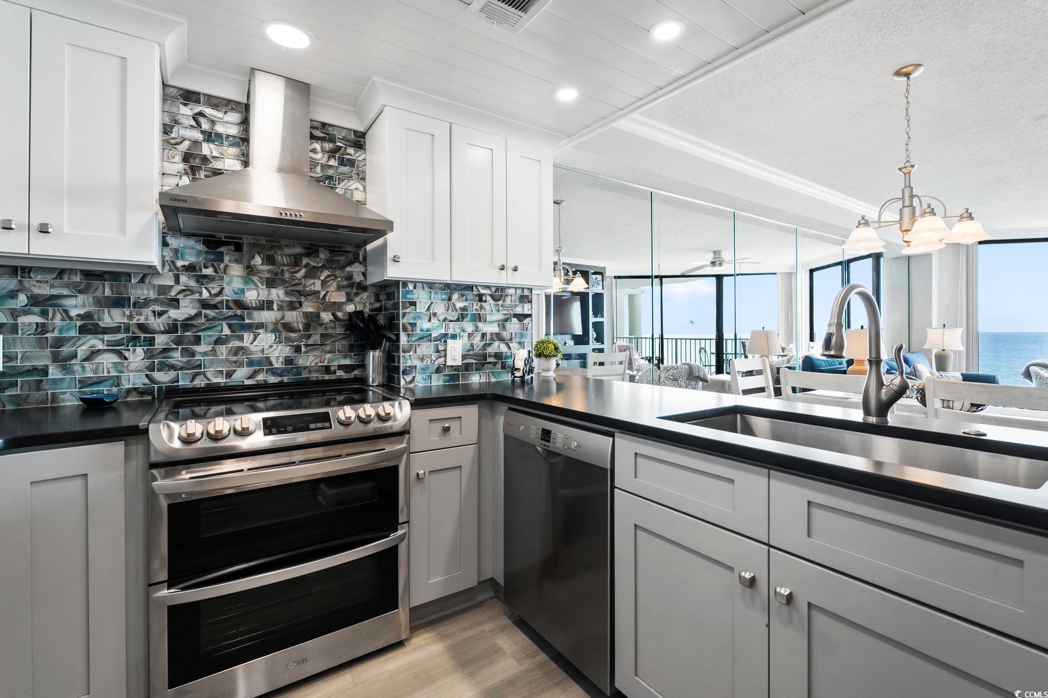 1990 North Waccamaw Drive, Unit 403 Murrells Inlet, SC 29576 - Photo 39 of 39 Kitchen with gray cabinets, stainless steel appliances, wall chimney range hood, tasteful backsplash, and open floor plan