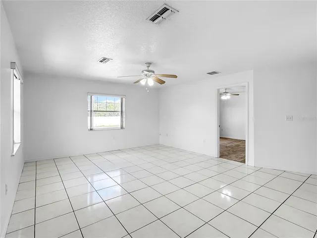 an empty room & chandelier fan and windows