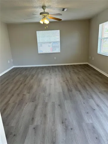 an empty room with wooden floor chandelier fan and windows