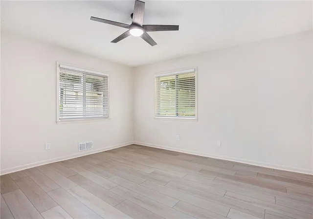 an empty room with wooden floor ceiling fan and windows