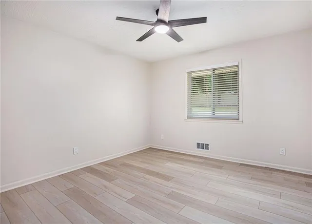 an empty room with wooden floor ceiling fan and windows