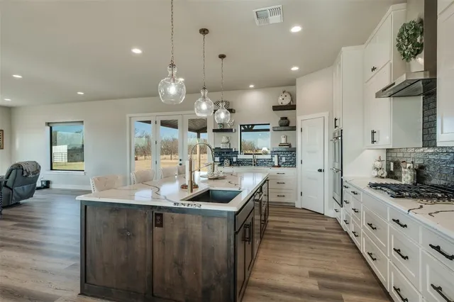 a kitchen with stainless steel appliances kitchen island granite countertop a sink a stove and a wooden floors