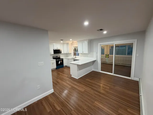 a large white kitchen with kitchen island a sink wooden floor and a refrigerator