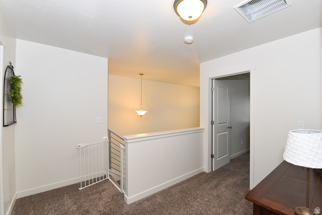 1632 North Apache Road Saratoga Springs, UT 84045 - Photo 14 of 28 Carpeted upper-level landing featuring a white painted railing with metal spindles, a flush-mount ceiling light, a recessed ceiling vent, and a hallway leading to an interior door