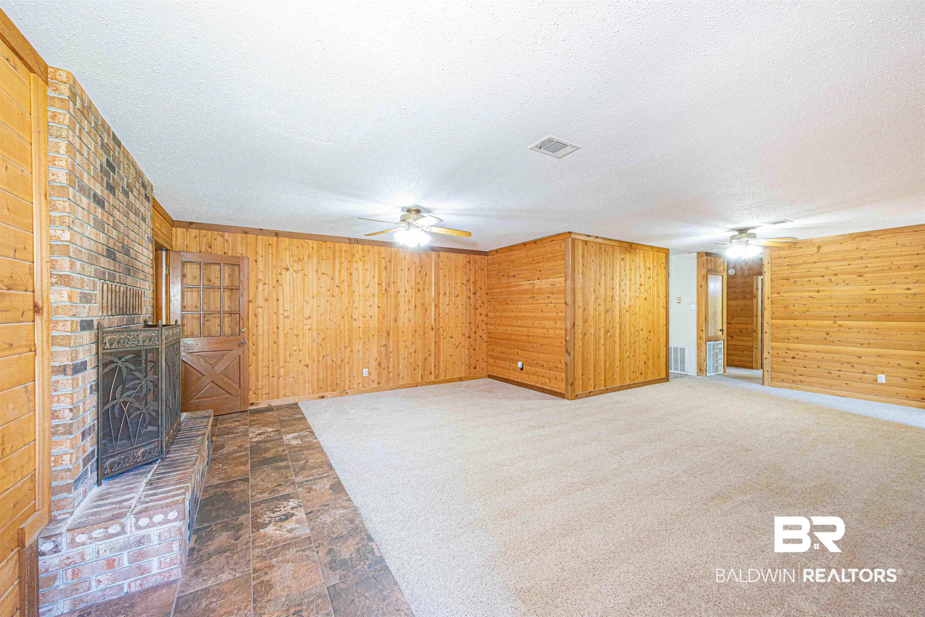 43101 Brown Road Bay Minette, AL 36507 - Photo 23 of 81 Unfurnished living room with ceiling fan, wooden walls, a brick fireplace, dark colored carpet, and dark stone finish flooring
