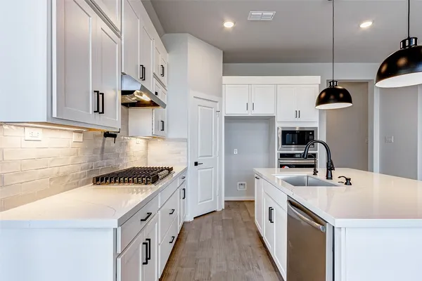 a kitchen with stainless steel appliances a sink a stove a refrigerator and white cabinets