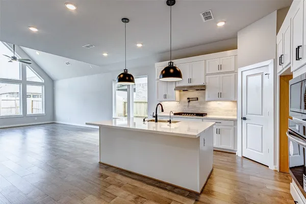 a kitchen with stainless steel appliances granite countertop a sink a stove a refrigerator and island with wooden floor