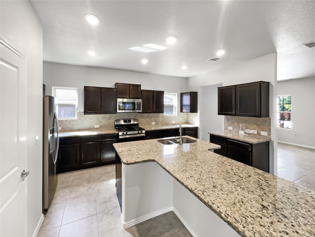 5709 Southerner Way Austin, TX 78747 - Photo 6 of 26 Kitchen with tasteful backsplash, light tile patterned floors, stainless steel appliances, dark brown cabinetry, and light stone countertops