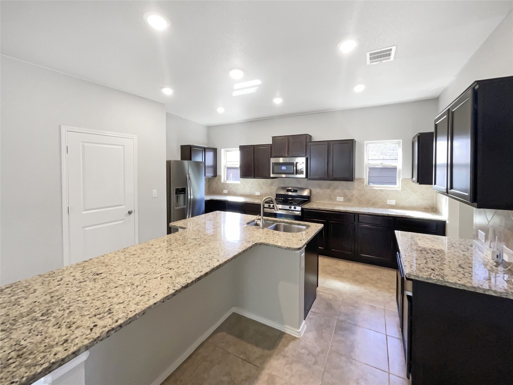 5709 Southerner Way Austin, TX 78747 - Photo 10 of 26 Kitchen featuring backsplash, stainless steel appliances, light stone countertops, light tile patterned floors, and healthy amount of natural light