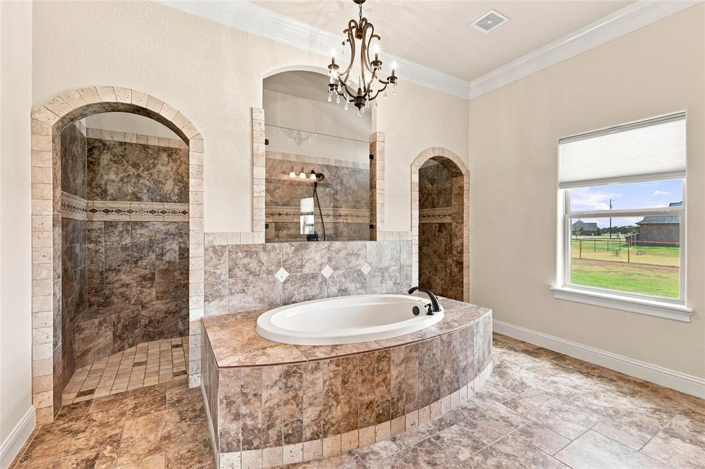 420 Hartley Way Azle, TX 76020 - Photo 17 of 40 Spacious bathroom featuring an oval soaking tub, two arched walk-in showers, decorative floor tiling, and an ornate chandelier