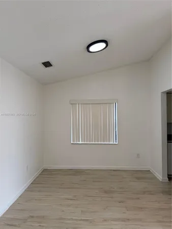 a view of an empty room with wooden floor and fan