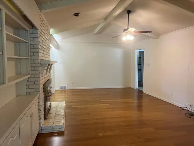 a view of an empty room with wooden floor and a ceiling fan