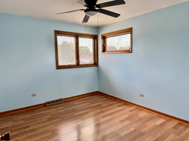 an empty room with wooden floor fan and windows