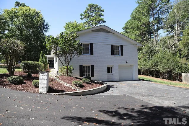 a view of a white house with a small yard and large trees