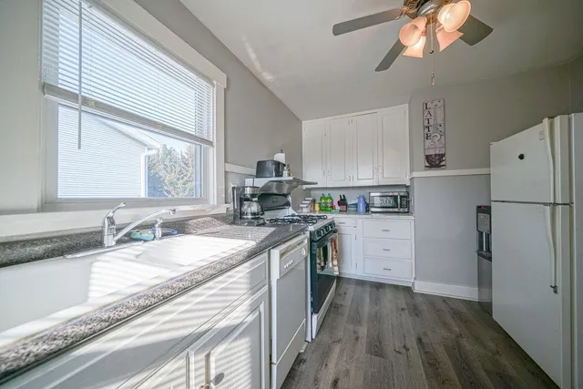 a kitchen with a sink dishwasher a refrigerator a stove and white cabinets with wooden floor