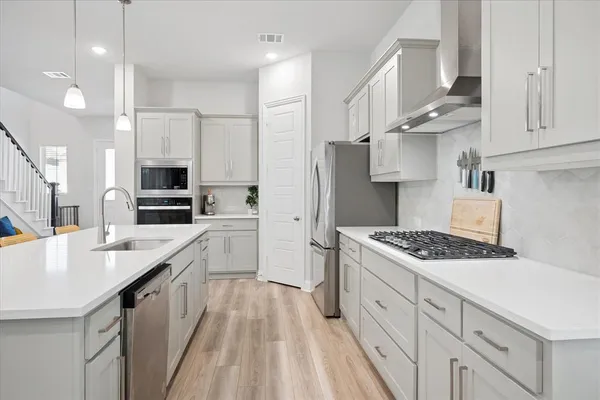 a kitchen with stainless steel appliances granite countertop a stove a sink dishwasher a refrigerator and white cabinets with wooden floor