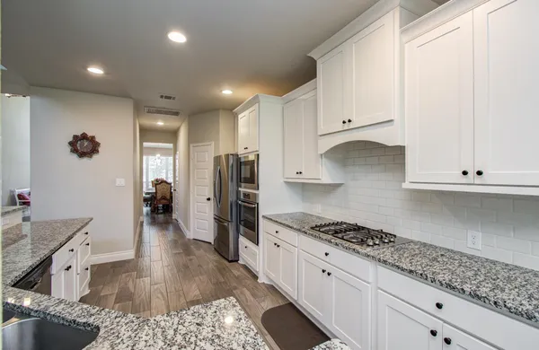 a large kitchen with stainless steel appliances kitchen island granite countertop a stove a sink dishwasher and a oven with white cabinets