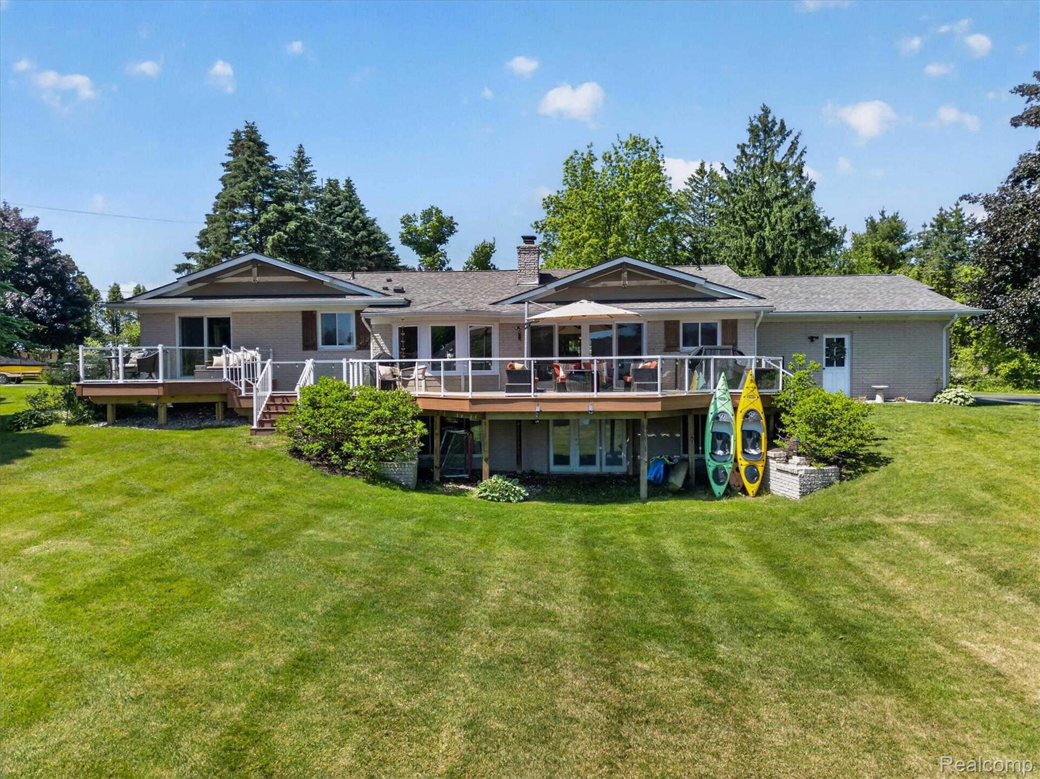 3860 East Commerce Road Commerce Township, MI 48382 - Photo 56 of 72 Expansive rear elevation featuring multiple elevated decks with glass panel railings, a lower-level walkout, and a spacious green lawn