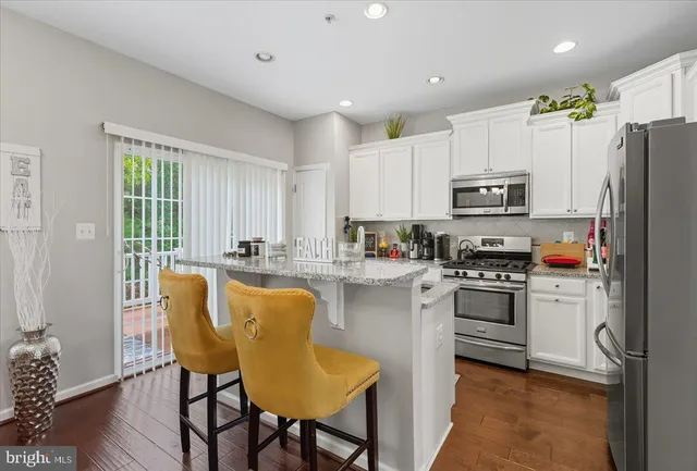 a kitchen with stainless steel appliances granite countertop a stove a sink a microwave a refrigerator and white cabinets with wooden floor