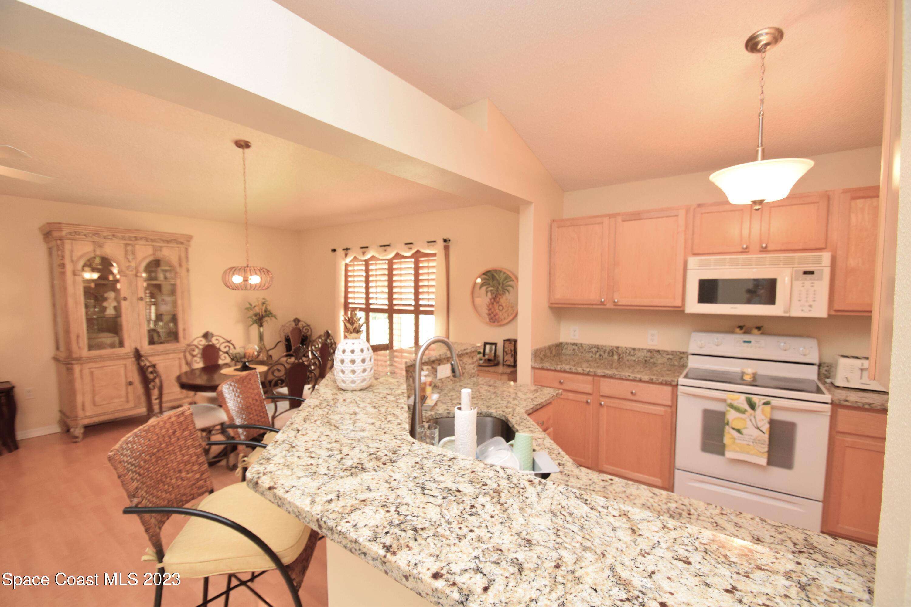2190 Spring Creek Circle Palm Bay, FL 32905 - Photo 62 of 73 a kitchen with stainless steel appliances kitchen island granite countertop a stove a sink a dining table and chairs with wooden floor