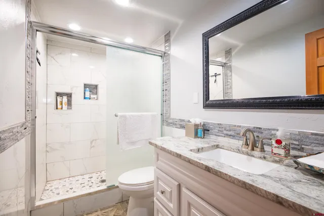 a bathroom with a granite countertop sink a toilet a mirror and shower