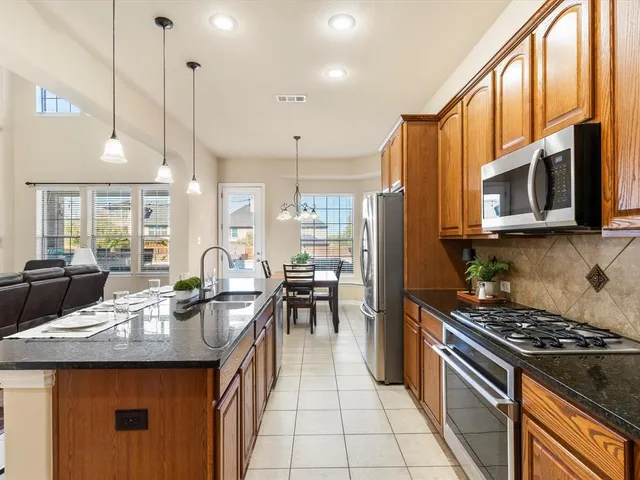 a kitchen with stainless steel appliances granite countertop a stove top oven a sink dishwasher a dining table and chairs with wooden floor