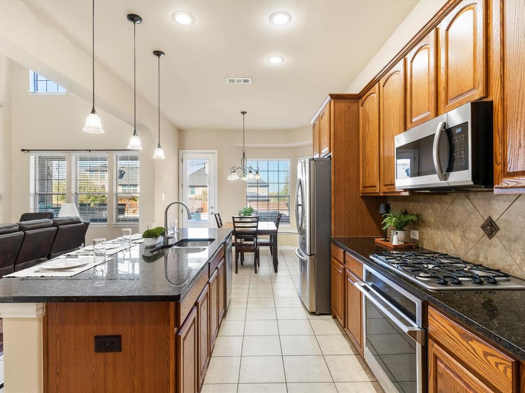 5365 Royal Lytham Road Fort Worth, TX 76244 - Photo 9 of 37 a kitchen with stainless steel appliances granite countertop a stove top oven a sink dishwasher a dining table and chairs with wooden floor