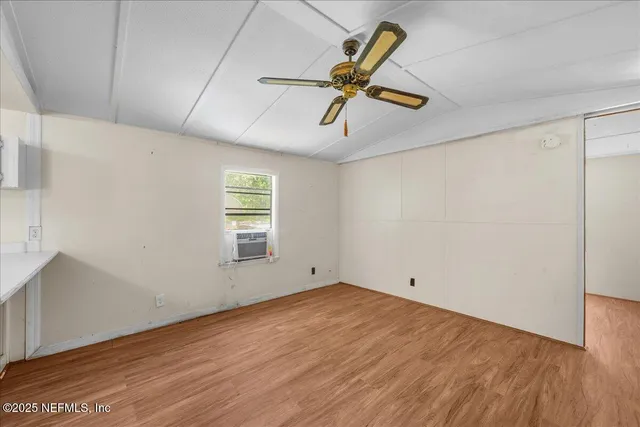 an empty room with wooden floor chandelier fan and windows