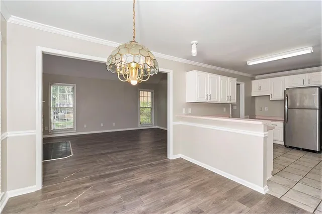 a view of a kitchen with a refrigerator a kitchen island wooden floor and a chandelier
