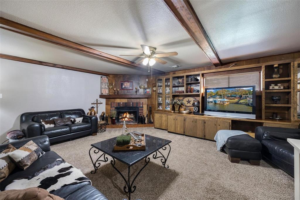 236 County Road 1422 Quitman, TX 75783 - Photo 5 of 34 Carpeted living area featuring a textured ceiling, a brick fireplace, beam ceiling, and a ceiling fan