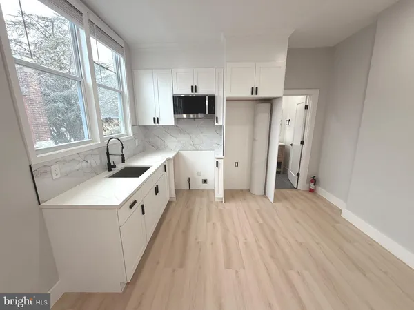 a large white kitchen with a sink a window and stainless steel appliances