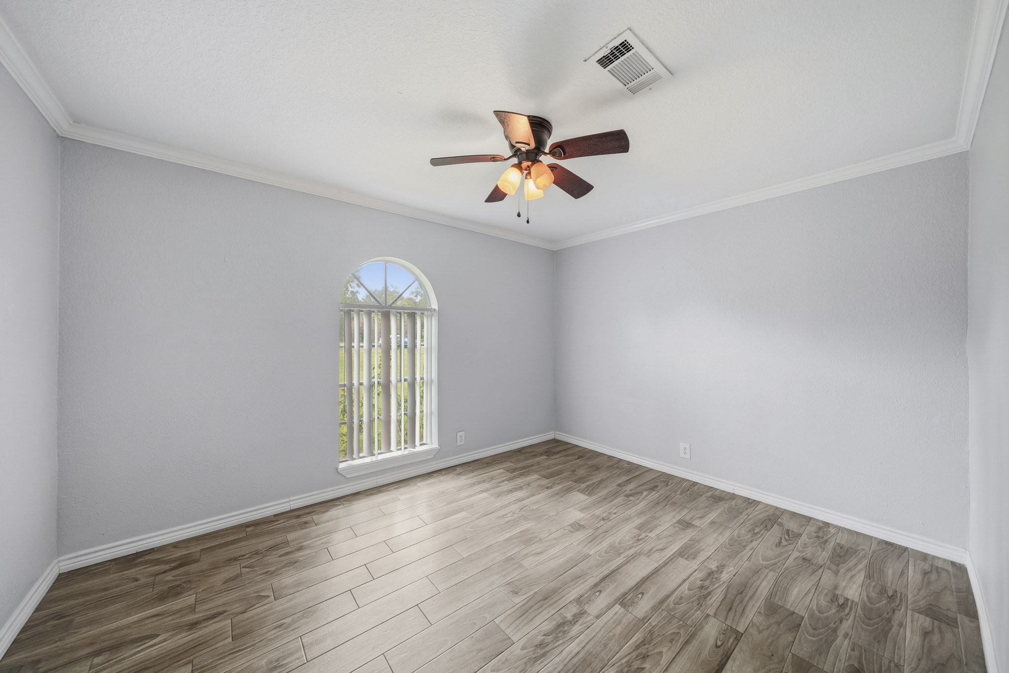 302 Country Road 893 Angleton, TX 77515 - Photo 17 of 26 Bright room with light gray walls and wood-look flooring. Features a large arched window allowing natural light and a ceiling fan for air circulation. Ideal for a bedroom or office space.