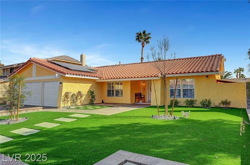 Back of property with solar panels, a tile roof, stucco siding, and a lawn
