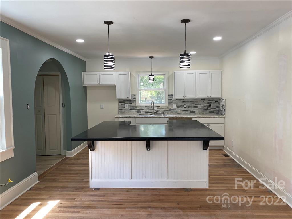 a kitchen with kitchen island granite countertop a sink cabinets and wooden floor
