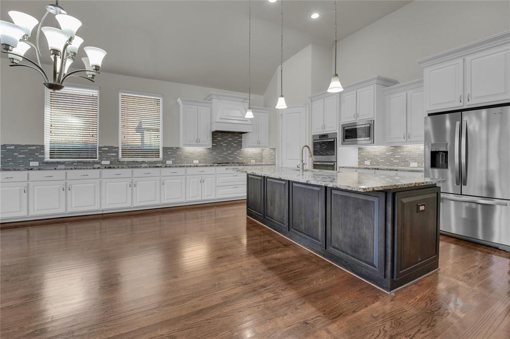 1011 Prairie Ridge Lane Arlington, TX 76005 - Photo 25 of 32 Spacious kitchen featuring a large central island with a stone countertop, extensive white cabinetry, stainless steel appliances, and wood-finish flooring