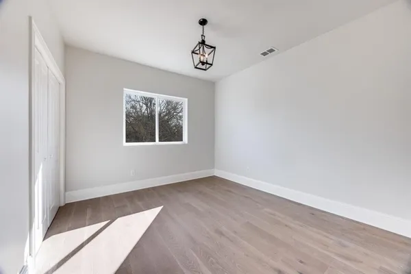 an empty room with wooden floor chandelier and windows