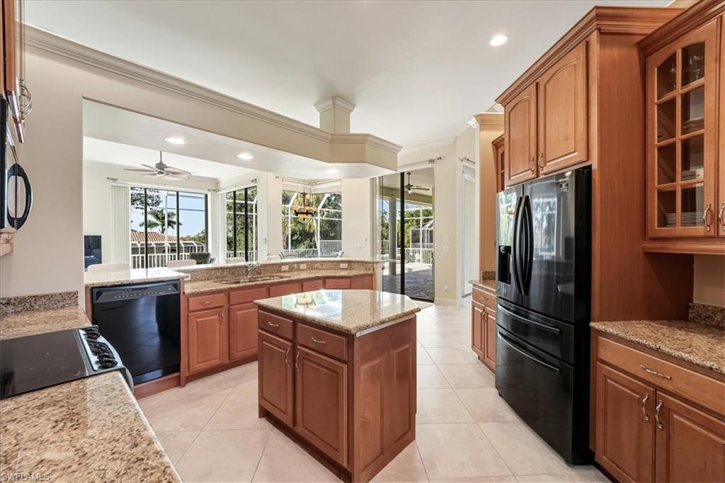 560 Inlet Drive Marco Island, FL 34145 - Photo 14 of 32 Kitchen featuring black appliances, brown cabinets, light stone counters, glass insert cabinets, and a kitchen island