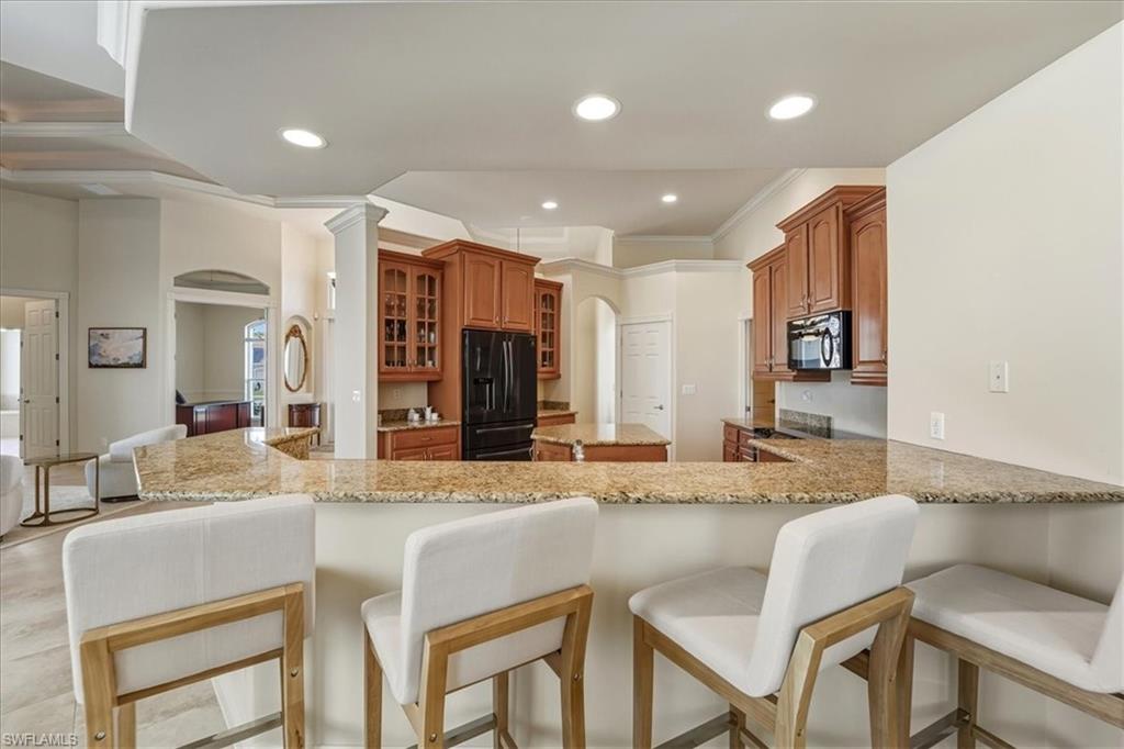 560 Inlet Drive Marco Island, FL 34145 - Photo 15 of 32 Kitchen featuring arched walkways, a breakfast bar, black appliances, light stone countertops, and brown cabinetry