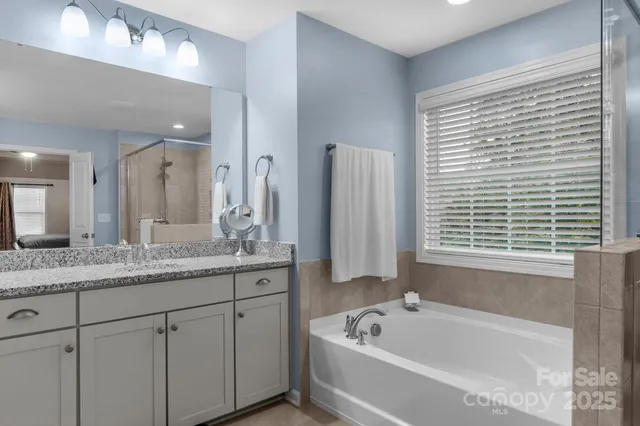 a bathroom with a granite countertop sink mirror bathtub and next to a window