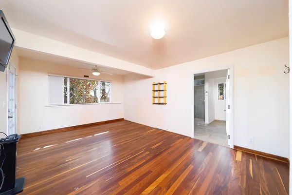 a view of an empty room with wooden floor and a ceiling fan