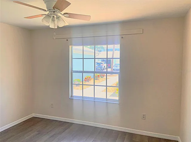 an empty room with wooden floor fan and windows