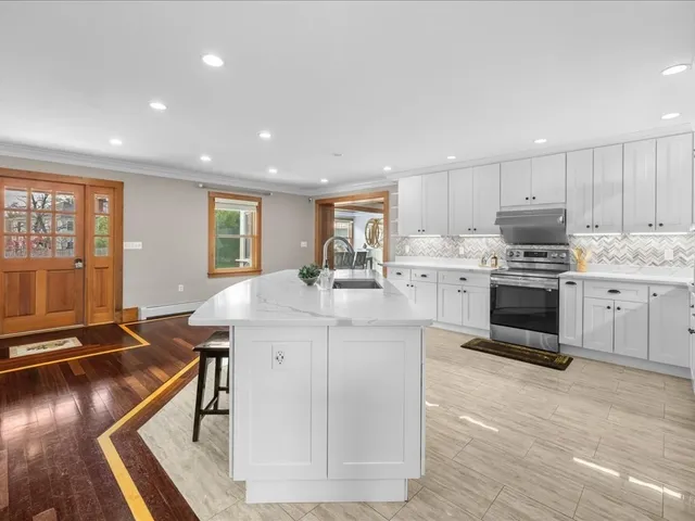a kitchen with kitchen island a stove a sink a refrigerator and a dining table with wooden floor