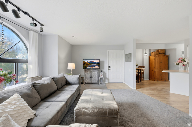 1175 Canyon Road, Unit 86 Ogden, UT 84404 - Photo 9 of 29 Spacious living area featuring a large arched window, track lighting, light gray wall paint, and mixed flooring with carpet and wood-finish