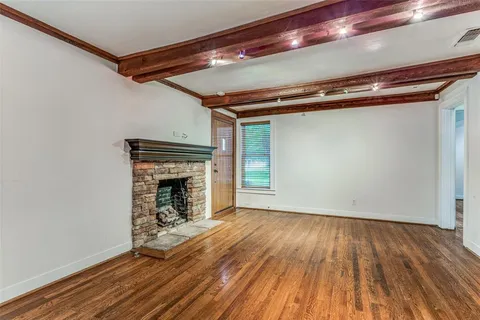 a view of an empty room with wooden floor a fireplace and a window